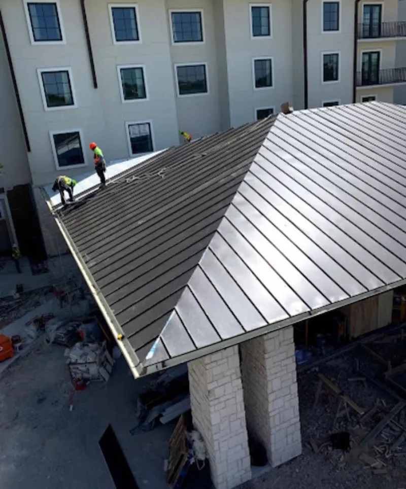 Crew installing standing seam metal roof panels on a commercial project in Benner